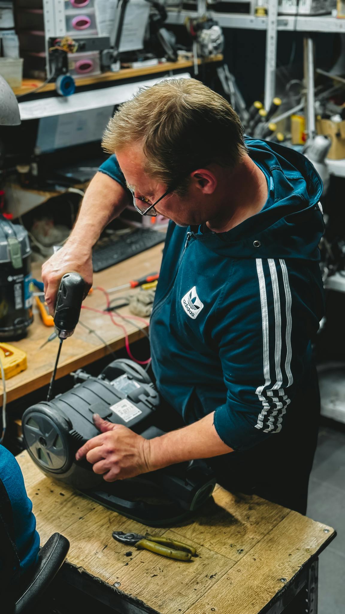 An adult male technician in a workshop using a power drill to repair machinery.